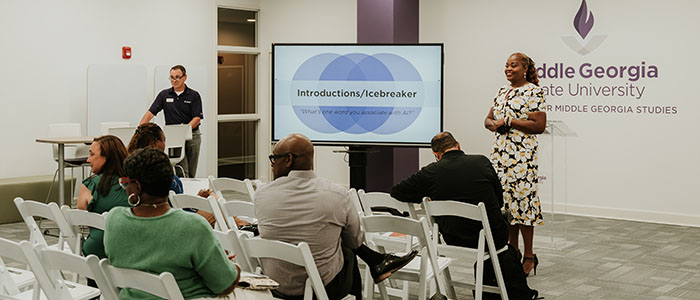 A presentation at the Center for Middle Georgia Studies, with speakers standing next to a large monitor displaying to the crowd.